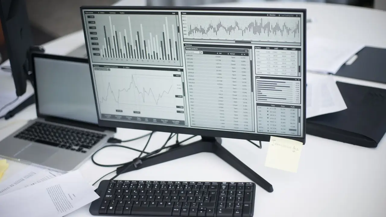 Curso de Access. Ordenador y portátil en una oficina con datos en pantalla.