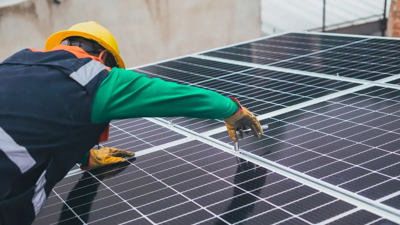 Curso de Diseño y Mantenimiento de Instalaciones de Energía Solar Fotovoltaica. Técnico con casco y guantes fijando paneles solares en una instalación fotovoltaica.